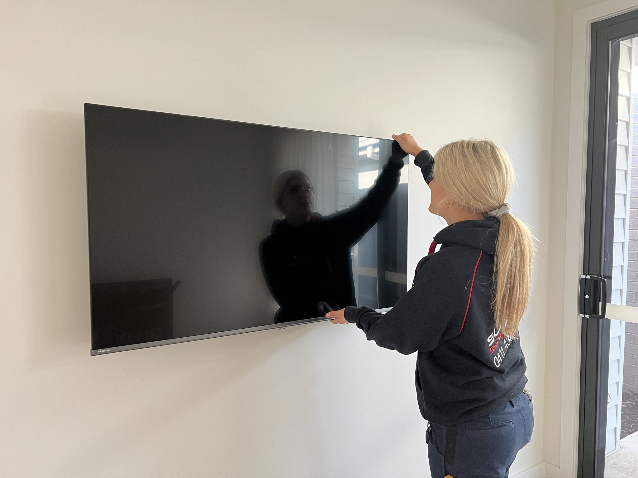 Electrician positioning TV after wall mounting on the wall.